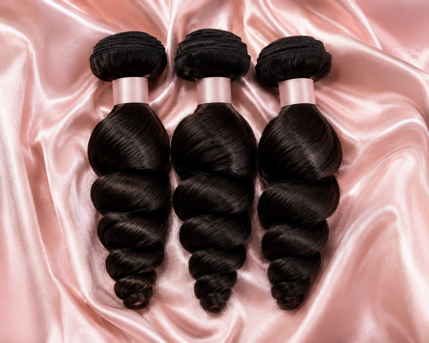 Loose wave raw hair bundles tied with blush ribbon on pink satin